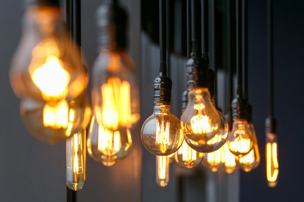 Vintage tungsten filament multiple lamps of different size and style hanging from the ceiling on a black wires as an interior design concept. Energy and design concept